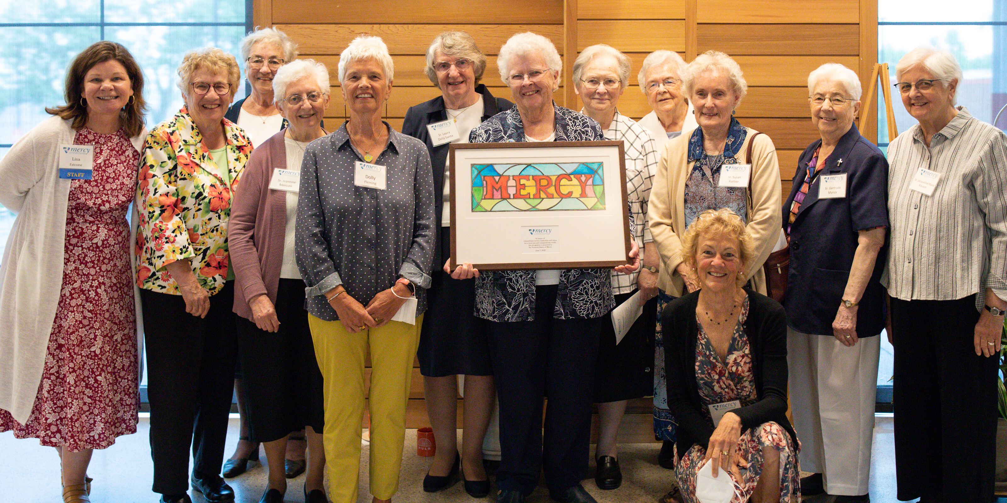 A large group of women, the Vermont Sisters of Mercy, with a framed painting of the word 