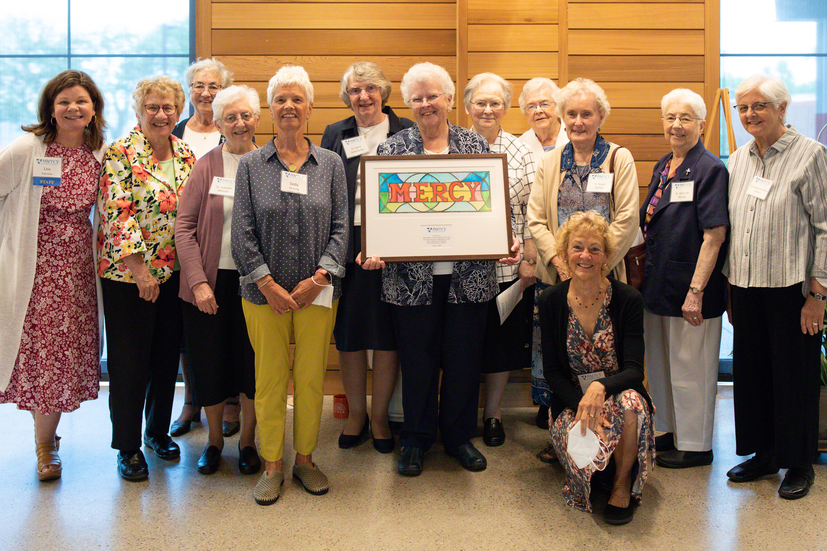 A large group of women, the Vermont Sisters of Mercy, with a framed painting of the word 